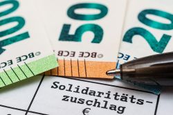 © Stockfotos-MG - stock.adobe.com Foto: Schriftzug Solidaritätszuschlag und Geldscheine